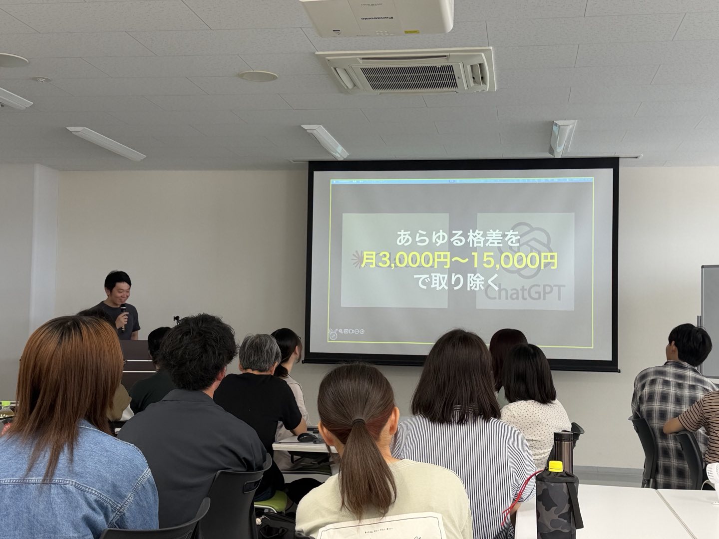 スクリーンに「あらゆる格差を 月3,000円〜15,000円 で取り除く」と映し出され、その前で話す様子