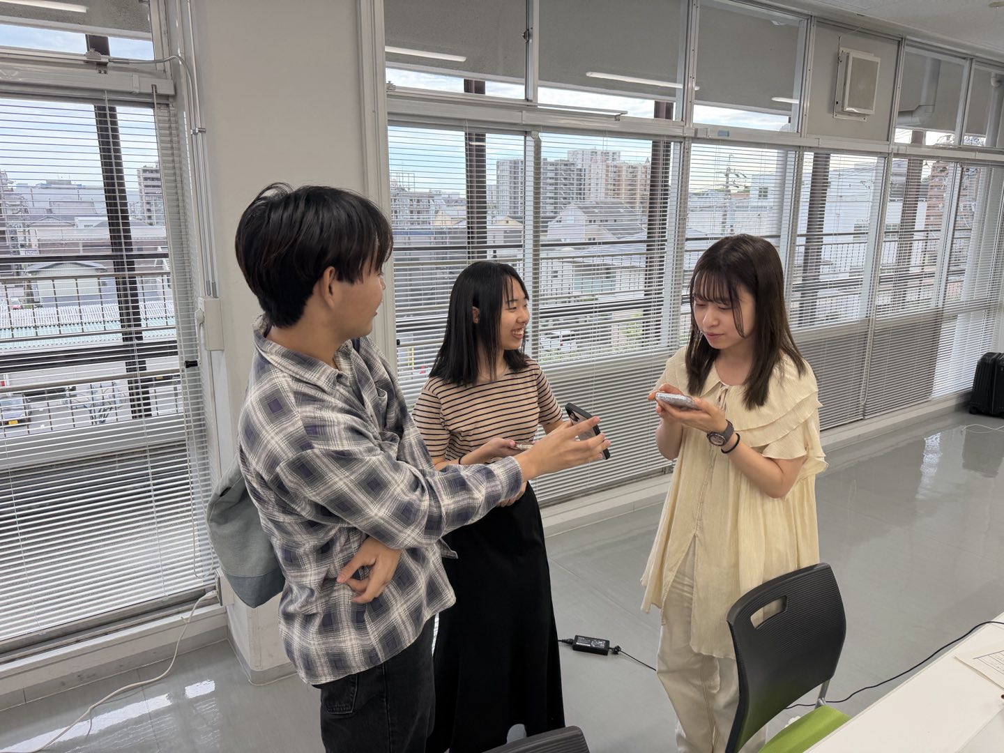 窓際に立った3人の参加者が、スマートフォンを手にしながら話し込んでいる様子
