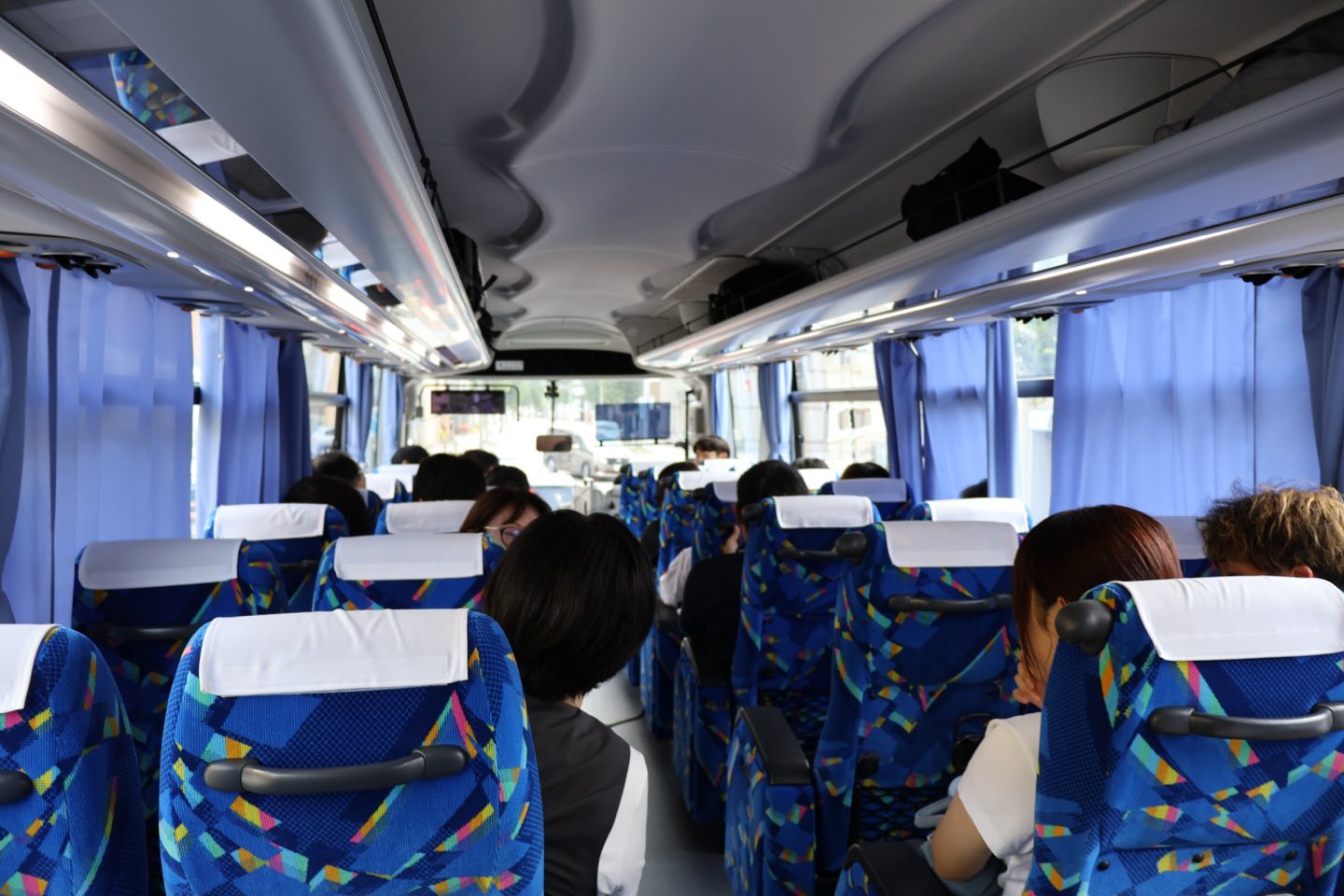 貸切バスの車内。座席に座った参加者たちが前方のガイドの話を聞いている