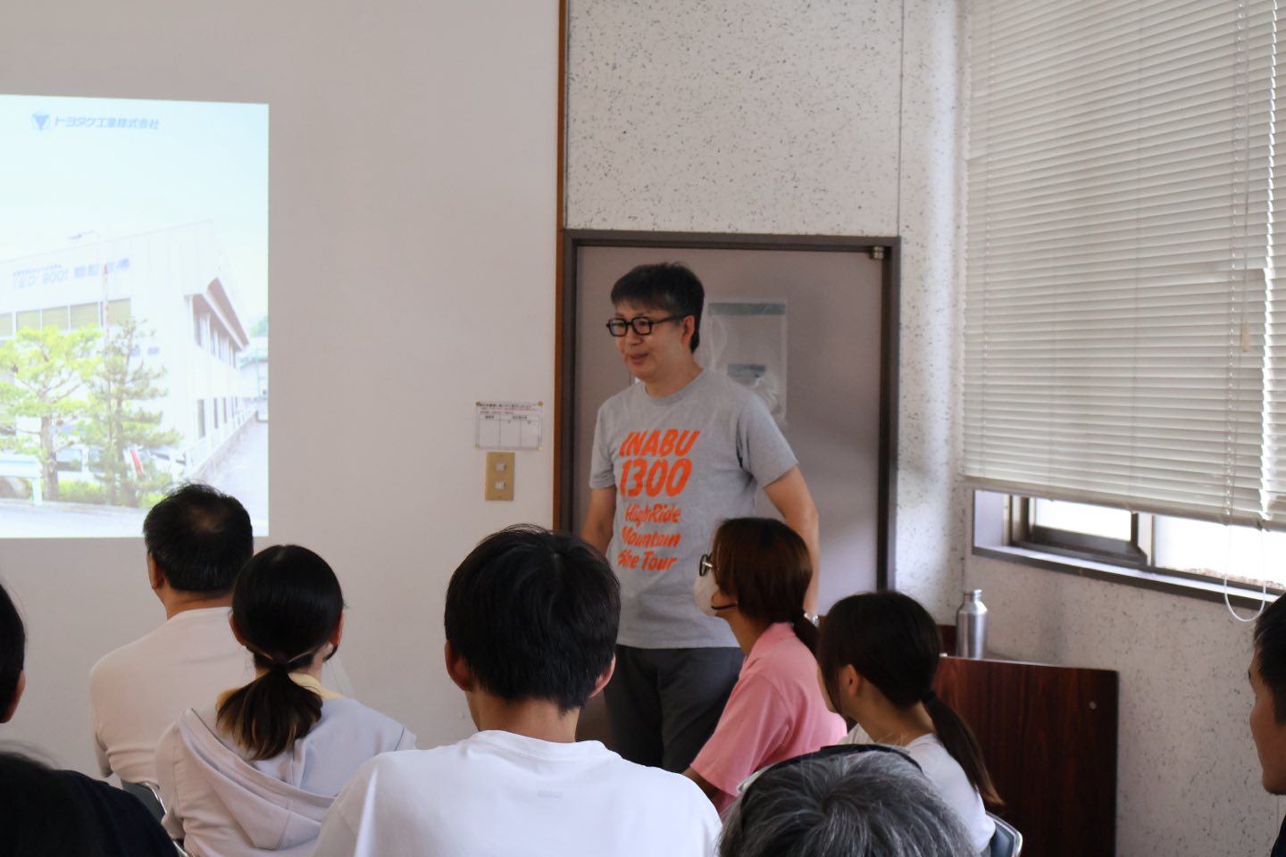 「INABU 1300」とプリントされたTシャツを着て、参加者の前で話すトヨタケ工業の横田幸史朗社長