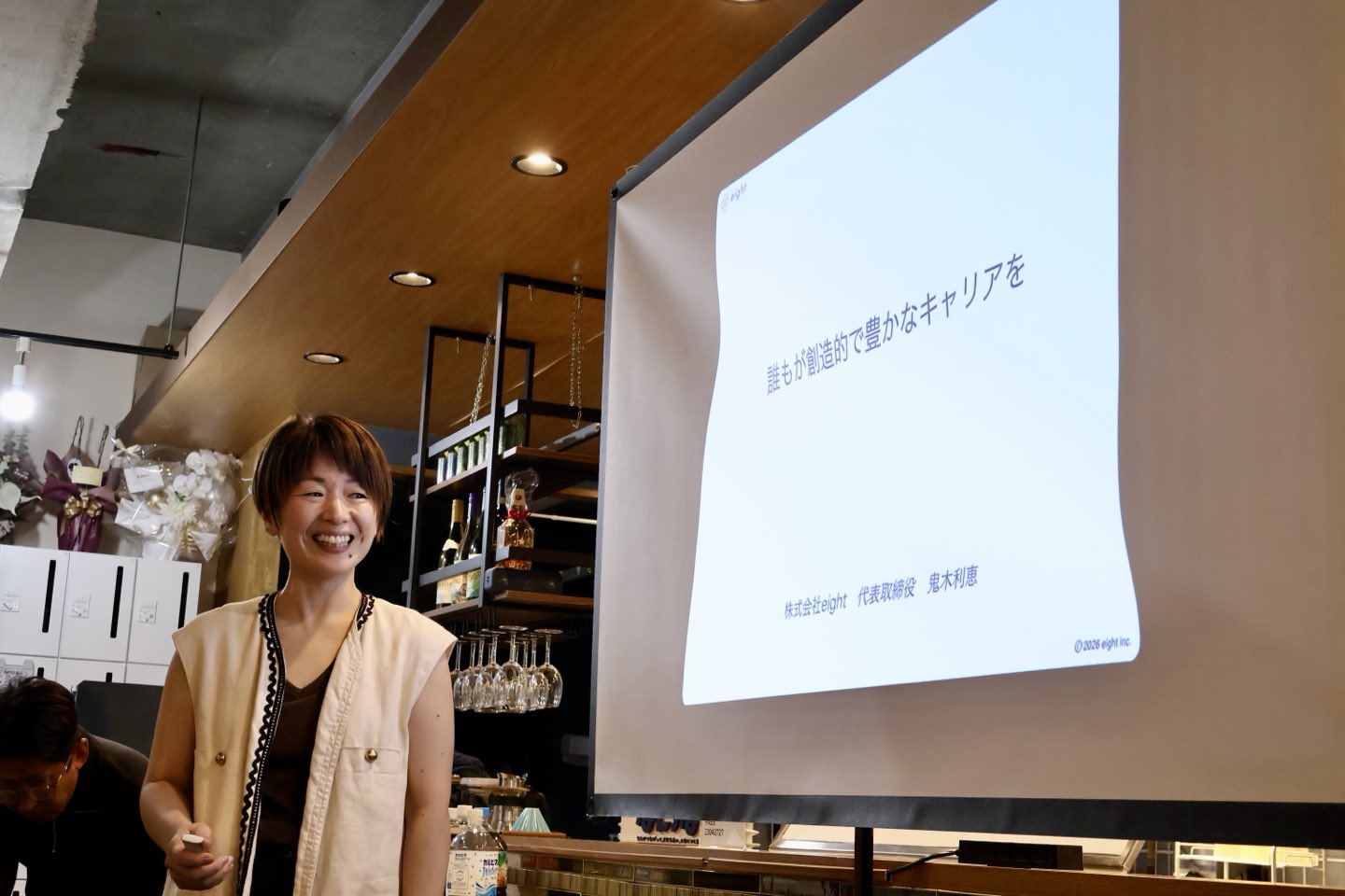 スクリーンの前に立ち、これまでの挑戦について話す株式会社eight代表の鬼木利瑛さん