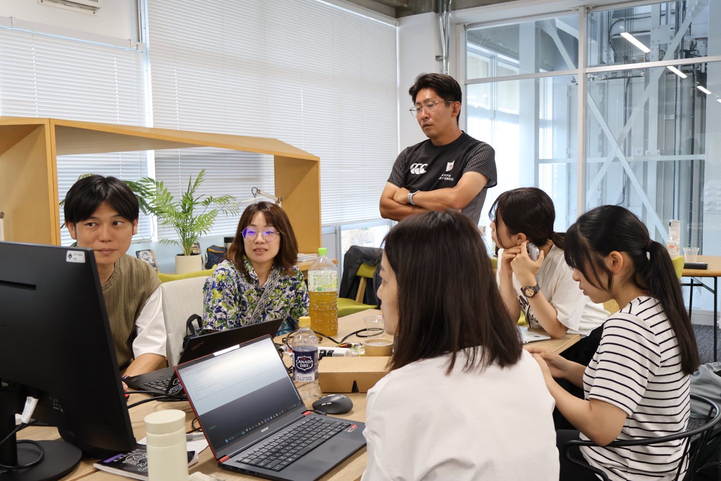 パソコンを開いて作業するチームのテーブルに立ち寄り、相談に応じるサポーター